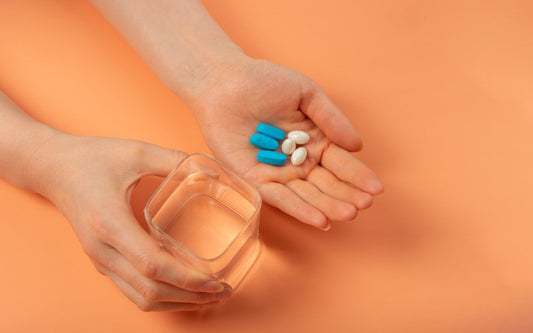 Hand holding assorted vitamins with a glass of water
