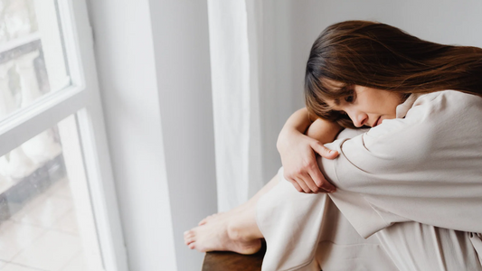 Woman hugging her knees by a window, feeling the low mood of seasonal depression