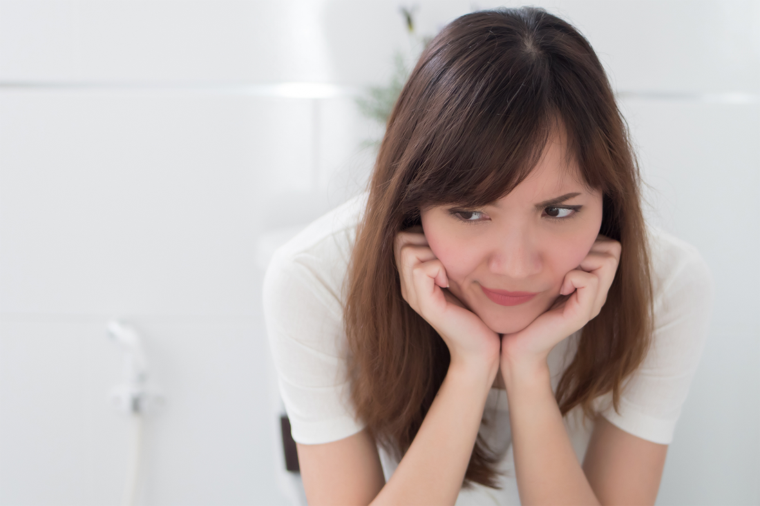 Woman sitting in the bathroom looking unamused, dealing with period digestion changes